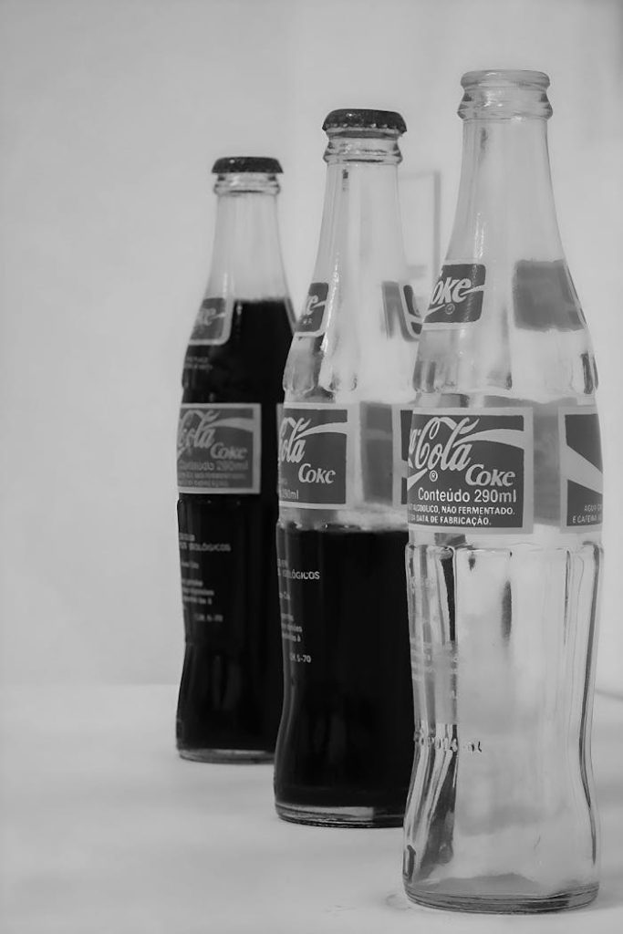 Artistic black and white image of Coca-Cola glass bottles with varying content levels.